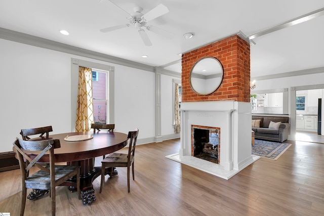 dining area with ceiling fan, a large fireplace, ornamental molding, and light wood-type flooring