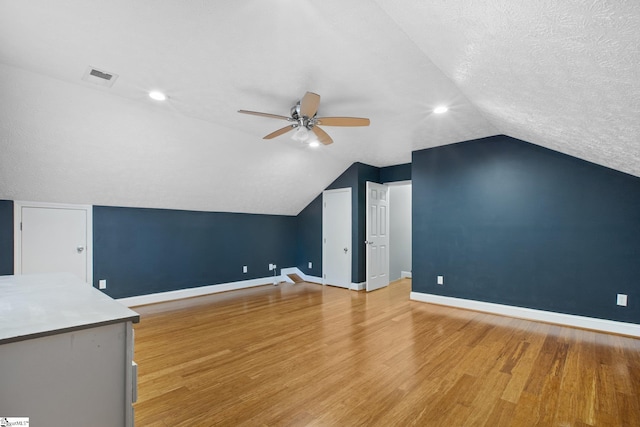 additional living space featuring a textured ceiling, hardwood / wood-style flooring, ceiling fan, and lofted ceiling