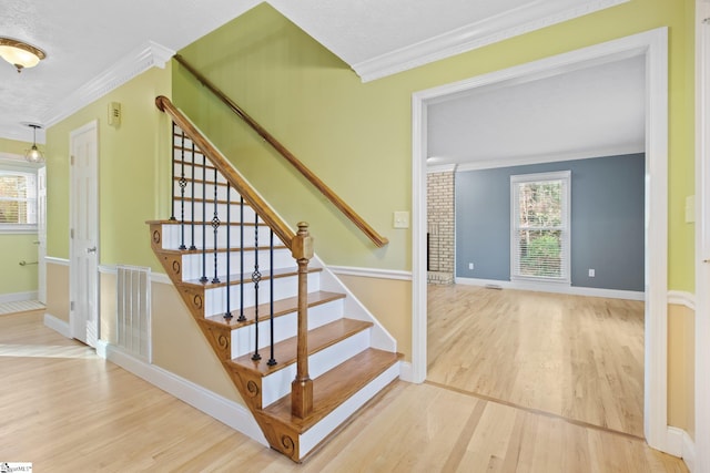 stairway with a wealth of natural light, wood-type flooring, and ornamental molding