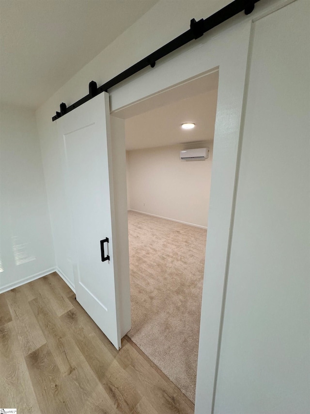 corridor with a wall unit AC, a barn door, and light hardwood / wood-style floors