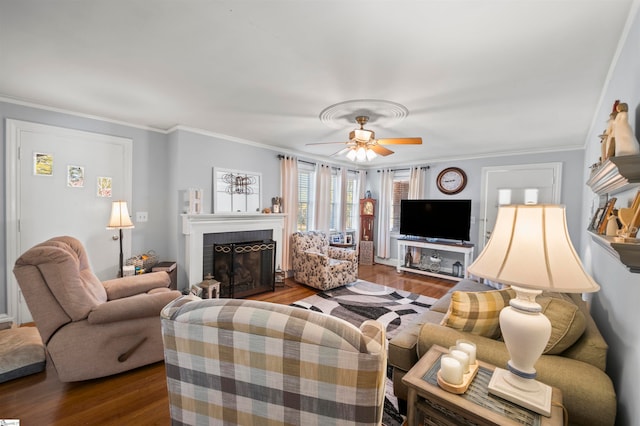 living room featuring hardwood / wood-style floors, ceiling fan, ornamental molding, and a brick fireplace