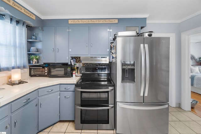 kitchen with tile counters, range hood, crown molding, light tile patterned floors, and appliances with stainless steel finishes