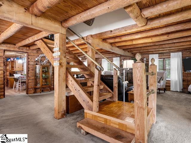 stairs with beam ceiling, wooden ceiling, carpet floors, and log walls