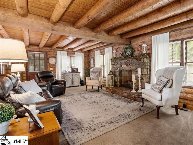 living area with beamed ceiling, a stone fireplace, a wealth of natural light, and wooden ceiling