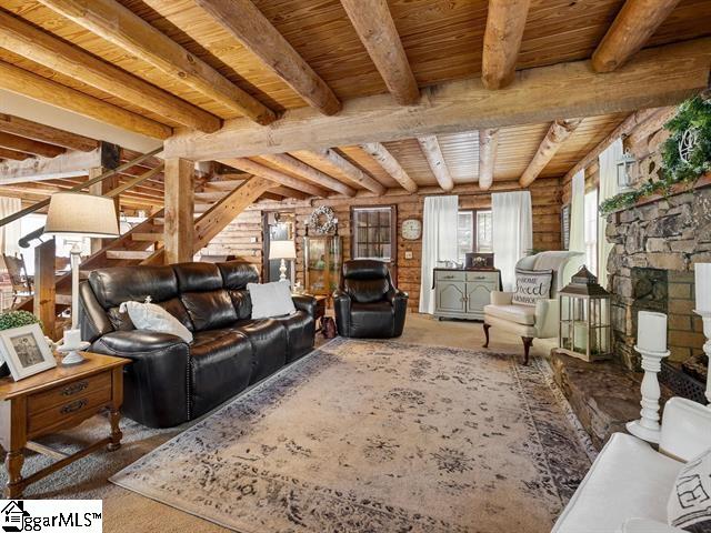 living room featuring beamed ceiling, a stone fireplace, and wooden ceiling