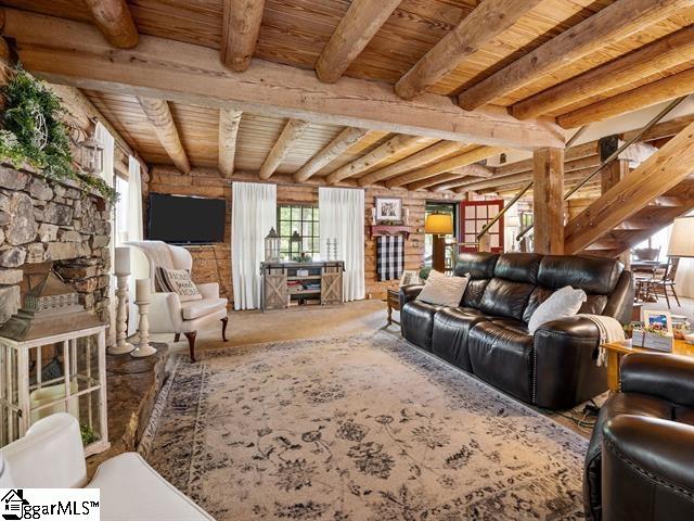 living room with a stone fireplace, beamed ceiling, and wood ceiling