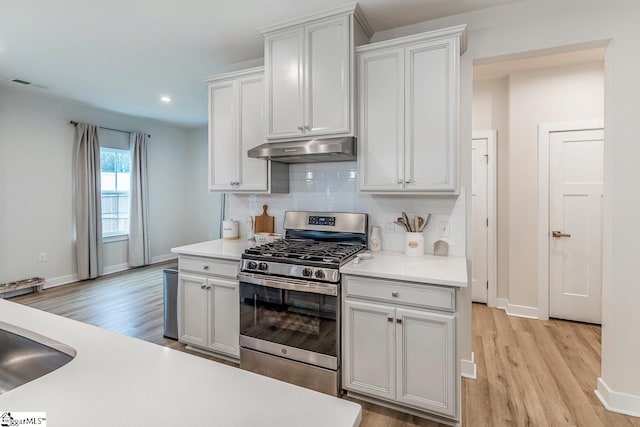 kitchen with backsplash, light hardwood / wood-style floors, stainless steel range with gas stovetop, and white cabinets