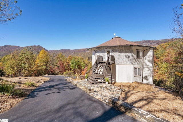 view of front facade with stone siding, a mountain view, a wooded view, and stairs