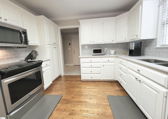 kitchen featuring backsplash, white cabinetry, light hardwood / wood-style flooring, and stainless steel appliances