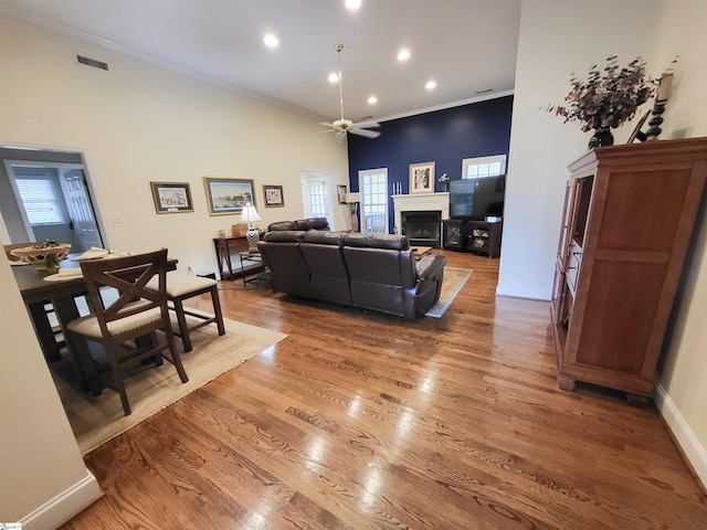 living room with ceiling fan, wood-type flooring, a towering ceiling, and crown molding