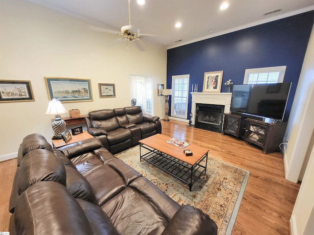 living room with ceiling fan, light hardwood / wood-style floors, crown molding, and a high ceiling