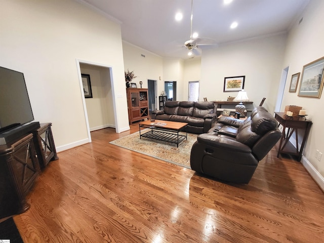 living room featuring a towering ceiling, crown molding, hardwood / wood-style floors, and ceiling fan