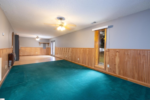 unfurnished room with ceiling fan, heating unit, carpet floors, a textured ceiling, and wooden walls