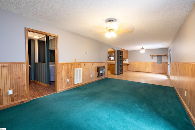 unfurnished living room with a textured ceiling, carpet floors, heating unit, and wood walls