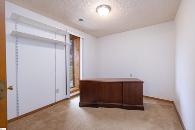 unfurnished office featuring a textured ceiling and light colored carpet