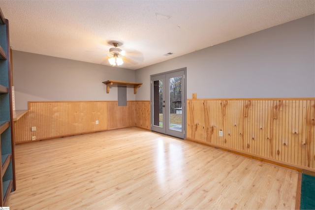 empty room featuring light wood-type flooring, a textured ceiling, wooden walls, and french doors