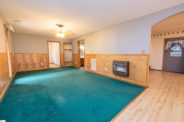 unfurnished room featuring wood walls, ceiling fan, a textured ceiling, wood-type flooring, and heating unit