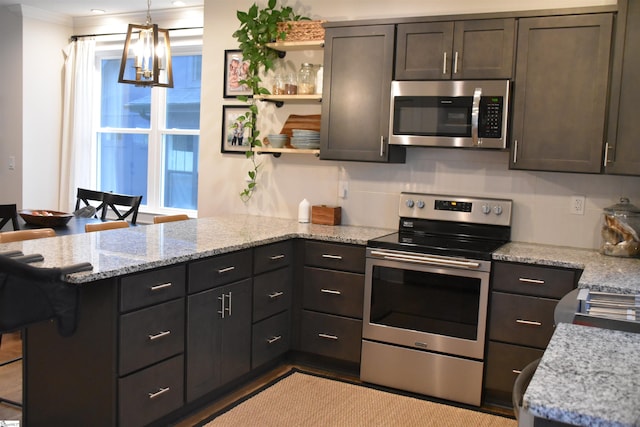 kitchen with appliances with stainless steel finishes, light stone counters, ornamental molding, dark brown cabinets, and a notable chandelier