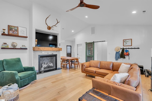 living room with hardwood / wood-style floors, a barn door, high vaulted ceiling, and ceiling fan