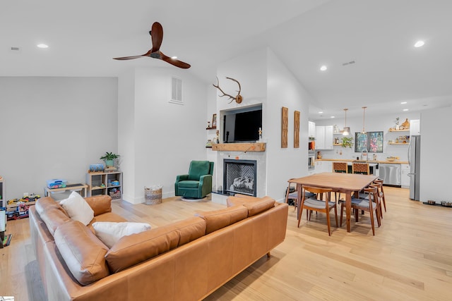 living room featuring light wood-type flooring, vaulted ceiling, ceiling fan, and sink