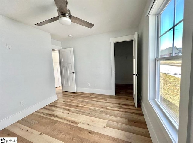 unfurnished bedroom with a walk in closet, ceiling fan, and light wood-type flooring