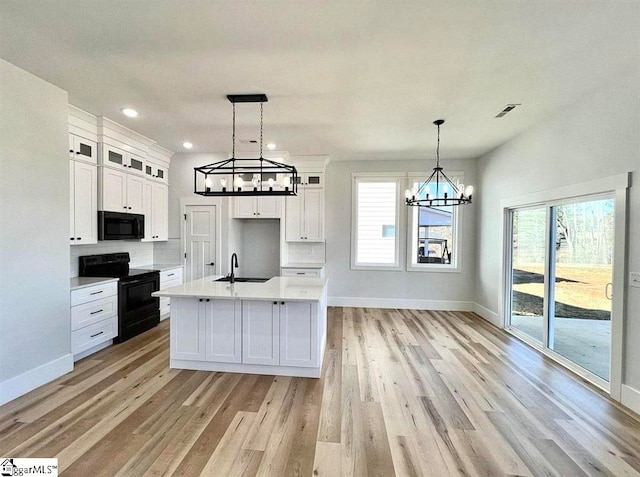 kitchen with sink, hanging light fixtures, a kitchen island with sink, white cabinets, and black appliances