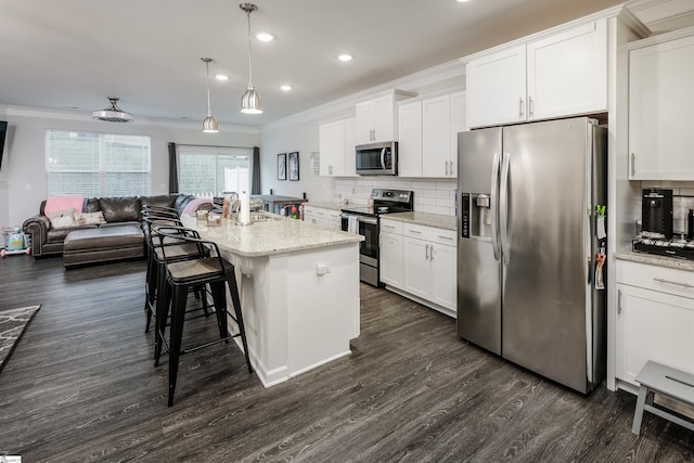 kitchen featuring hanging light fixtures, crown molding, a center island with sink, white cabinets, and appliances with stainless steel finishes