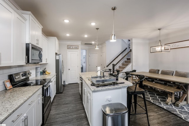 kitchen with white cabinets, hanging light fixtures, a kitchen island with sink, and appliances with stainless steel finishes