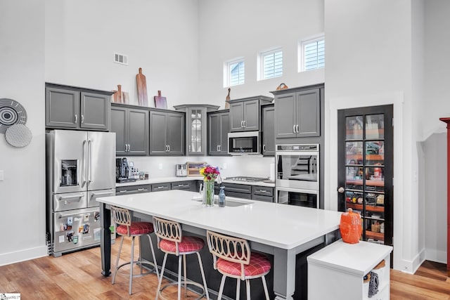 kitchen with a kitchen bar, light hardwood / wood-style flooring, a high ceiling, and appliances with stainless steel finishes