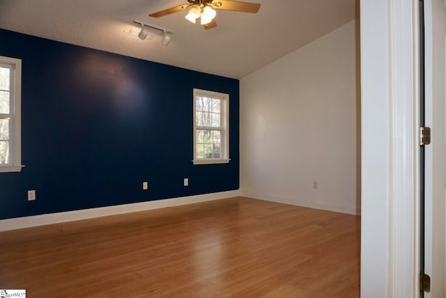 empty room featuring ceiling fan, rail lighting, vaulted ceiling, and light wood-type flooring