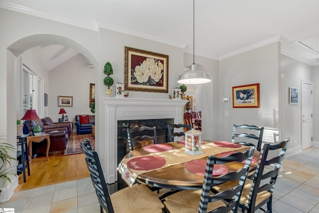 dining area featuring a premium fireplace, crown molding, light tile patterned flooring, and lofted ceiling