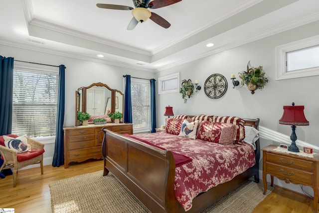 bedroom with a tray ceiling, ceiling fan, ornamental molding, and light wood-type flooring