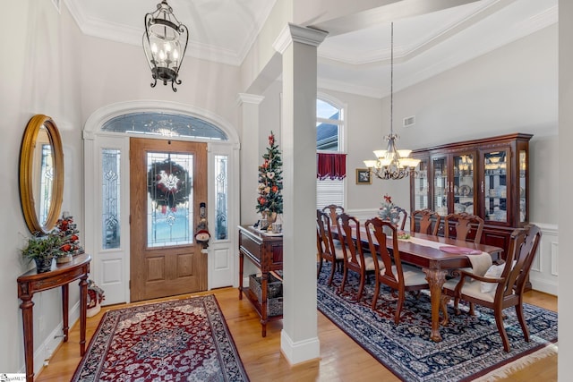 entrance foyer featuring decorative columns, ornamental molding, light hardwood / wood-style flooring, a chandelier, and a high ceiling