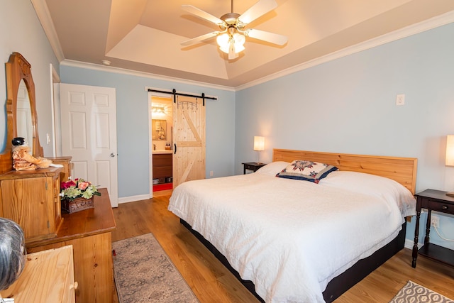 bedroom featuring ceiling fan, a barn door, ensuite bathroom, hardwood / wood-style flooring, and ornamental molding