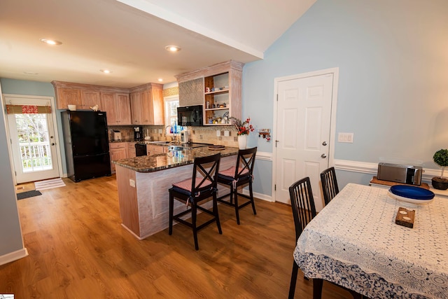 kitchen with kitchen peninsula, a kitchen breakfast bar, light wood-type flooring, tasteful backsplash, and black appliances