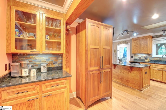 kitchen with tasteful backsplash, light hardwood / wood-style flooring, crown molding, and dark stone countertops