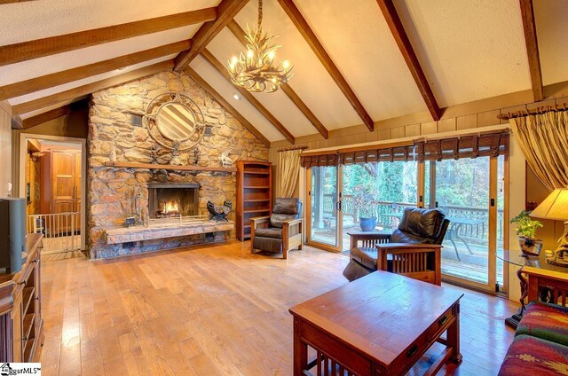 living room featuring an inviting chandelier, a stone fireplace, lofted ceiling with beams, wood-type flooring, and a textured ceiling