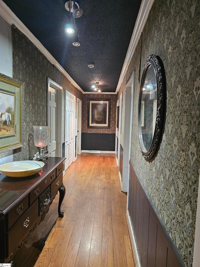 corridor with a textured ceiling, light hardwood / wood-style floors, and ornamental molding