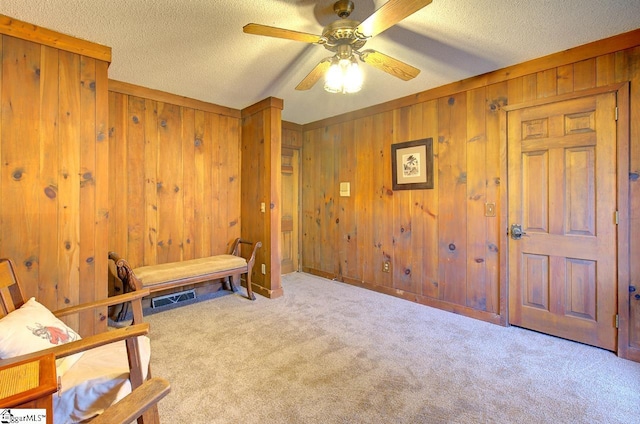 sitting room featuring ceiling fan, wood walls, a textured ceiling, and light carpet