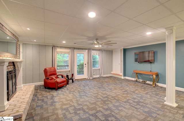 living area featuring a paneled ceiling, ceiling fan, and a brick fireplace