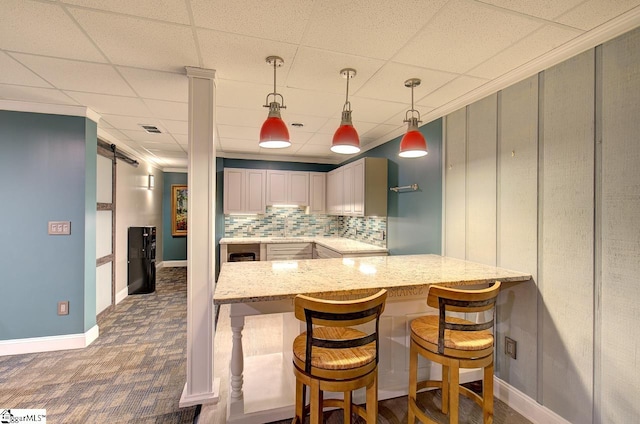 kitchen with kitchen peninsula, a barn door, a drop ceiling, and pendant lighting