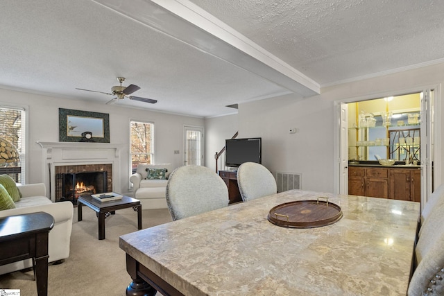 dining space with beam ceiling, ceiling fan, a textured ceiling, light carpet, and ornamental molding