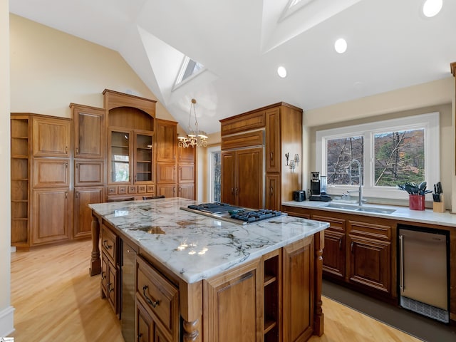 kitchen featuring lofted ceiling with skylight, sink, light hardwood / wood-style flooring, a kitchen island, and stainless steel gas cooktop