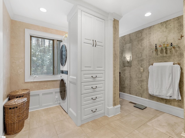 laundry area featuring light tile patterned floors, stacked washer and dryer, and crown molding