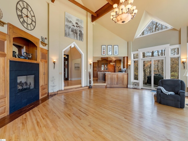 unfurnished living room with high vaulted ceiling, a tiled fireplace, light hardwood / wood-style flooring, beam ceiling, and a chandelier