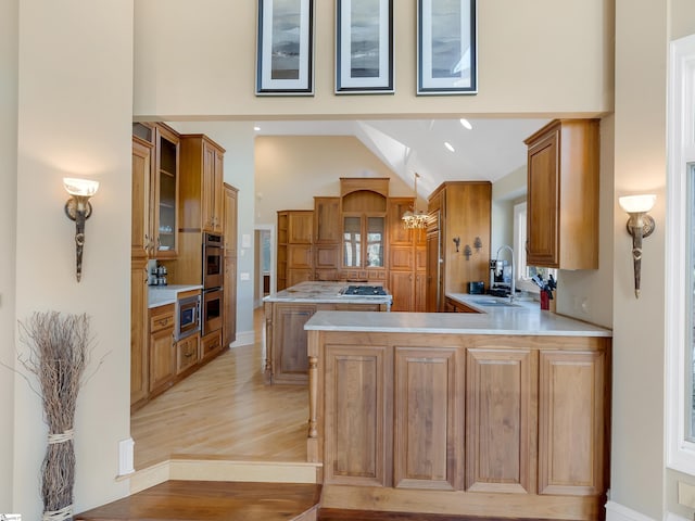 kitchen featuring sink, stainless steel double oven, high vaulted ceiling, kitchen peninsula, and light wood-type flooring