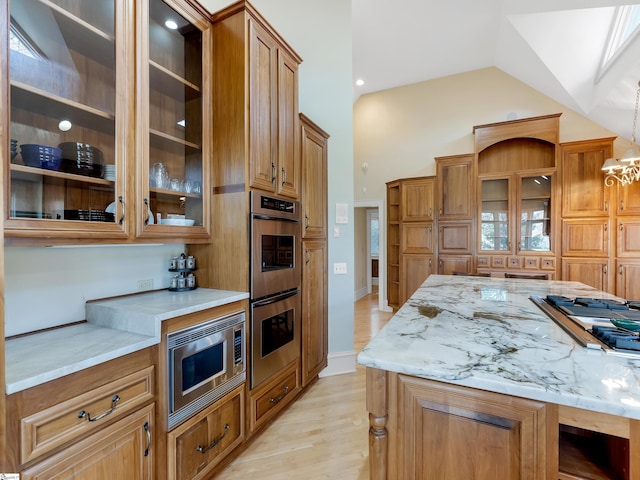 kitchen with light stone countertops, stainless steel appliances, decorative light fixtures, lofted ceiling, and light wood-type flooring