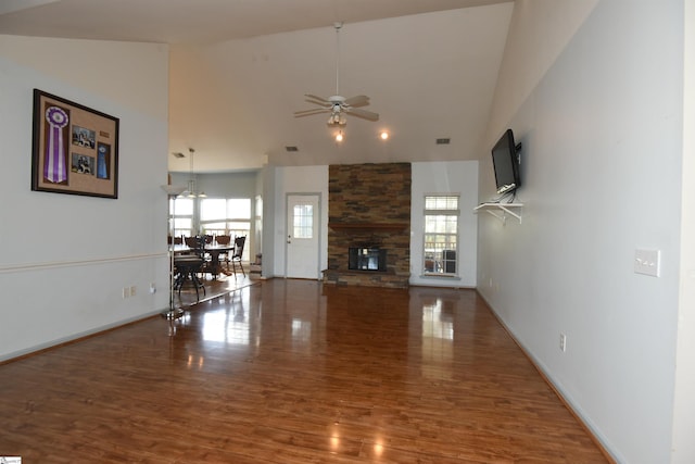 unfurnished living room featuring hardwood / wood-style floors, high vaulted ceiling, a stone fireplace, and ceiling fan