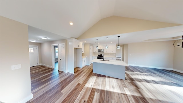 kitchen featuring stainless steel appliances, vaulted ceiling, a kitchen island, light hardwood / wood-style flooring, and white cabinetry