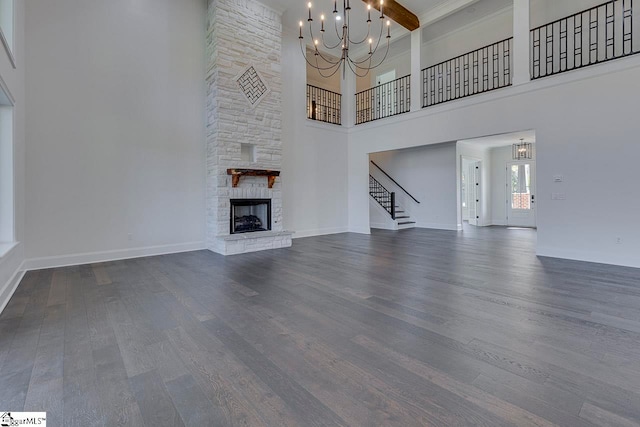 unfurnished living room with a high ceiling, a stone fireplace, dark wood-type flooring, and a notable chandelier